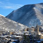 Panorama del paese abruzzese con colline verdi e cielo blu, ideale per passeggiate all'aria aperta.