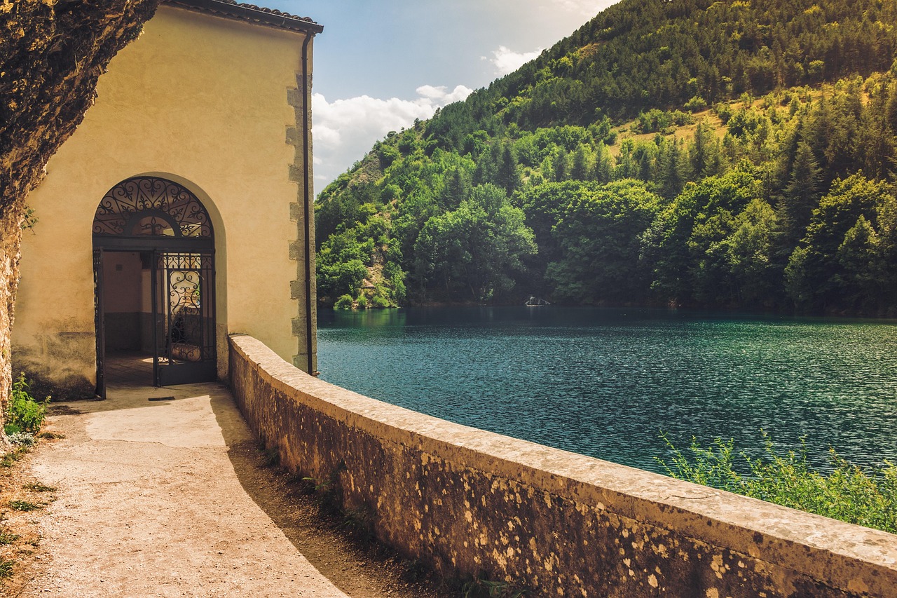Lago di Vico circondato da alberi, con riflessi dell'acqua e cielo sereno, evocando la leggenda di Ercole.