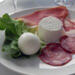 Mozzarella di bufala fresca su un tagliere, circondata da fattorie e paesaggi campani.