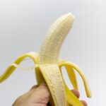 Una mano tiene una banana matura su sfondo bianco, simbolo di salute e benessere.
